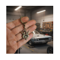 V8 Schlüsselanhänger aus Messing in der Werkstatt Hand hält V8 Schlüsselanhänger aus Messing vor einem Muscle‑Car in der Werkstatt.