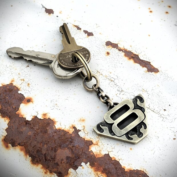 V8 Schlüsselanhänger – Messing, Flammen-Design V8-Anhänger aus massivem Messing mit Flammen, fotografiert auf klassischer Motorhaube; für Muscle-Car-Fahrer