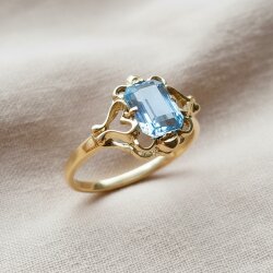 Filigraner 14k Goldring mit achteckig facettiertem hellblauem Aquamarin in ornamentaler Krappenfassung, Vintage-Stil auf hellem Leinenstoff