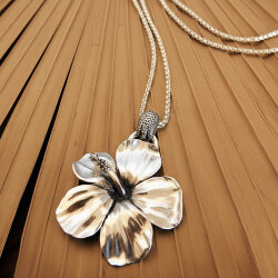 Handgefertigter Silberanhänger in Form einer Hibiskusblüte mit detaillierten Blütenblättern und Stempel mit Silberkette, auf hellem Holzuntergrund